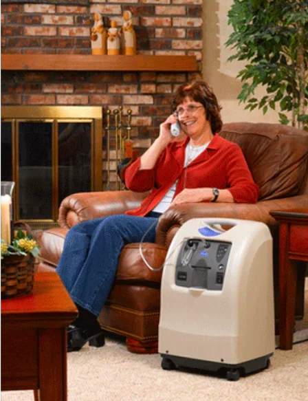 Woman sitting on a couch with a portable oxygen concentrator in a living room.
