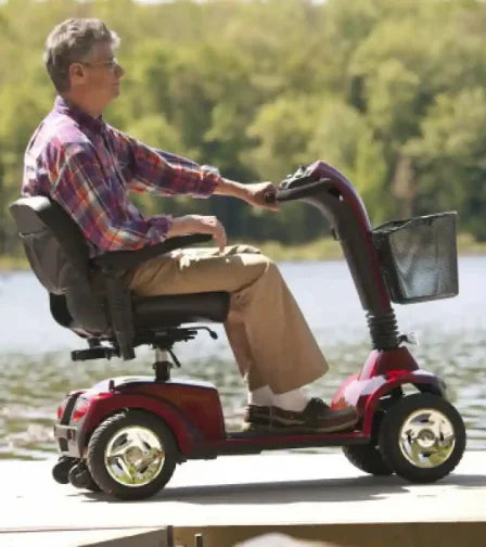 Man riding a mobility scooter by a lake with trees in the background